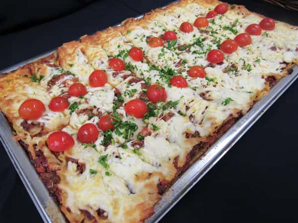 Oven baked dish topped with melted cheese served in the pan and garnished with cherry tomatoes and parsley