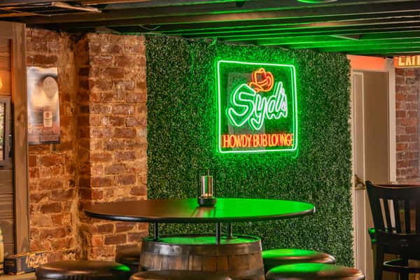 Interior exposed brick and stylish wall with greenery and a neon Syd's Bar & Grill sign