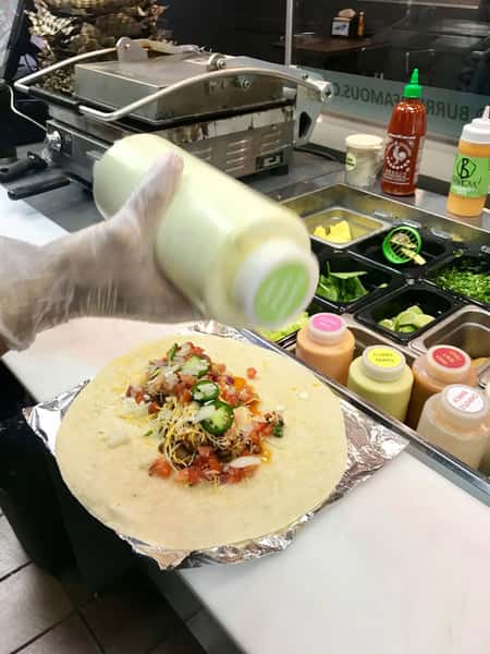 Fresh burrito being prepared at Burrito Famous with seasoned meat, pico de gallo, jalapeños, shredded cheese, and house sauce in an open kitchen.