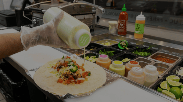 Burrito Famous chef preparing a fresh burrito with house-made sauce, pico de gallo, jalapeños, and premium ingredients in the restaurant's open kitchen.