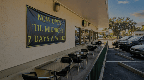 Outdoor patio seating at Burrito Famous with café tables, chairs, and a sign announcing the restaurant is open until midnight seven days a week.