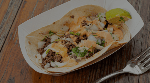 Soft taco filled with seasoned ground beef, melted cheese, fresh onions, cilantro, creamy chipotle sauce, and a lime wedge from Burrito Famous.