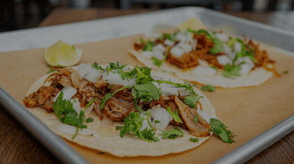 Two authentic pork street tacos topped with fresh cilantro and diced onions, served with lime wedges on a tray at Burrito Famous.