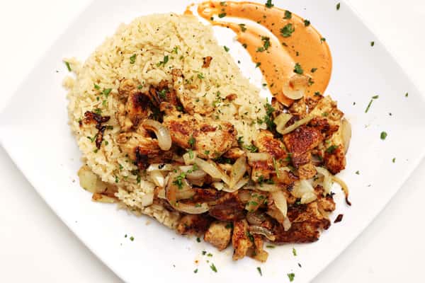 Here is a plate of delicious food. It's likely a Mediterranean dish with rice, chicken or lamb, onions, herbs, and a flavorful sauce.