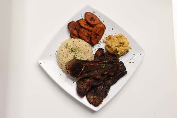 A top-down shot showcases a square plate with an assortment of food items, including meat, fried plantains, rice, and a side of vegetables. This photo is used in the website gallery to highlight menu items.