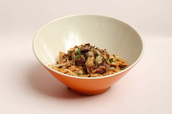 A bowl of Nashville's Hottest Chicken and pasta sits ready to be savored in a cream and orange bowl. The pasta is topped with chopped greens and onions.