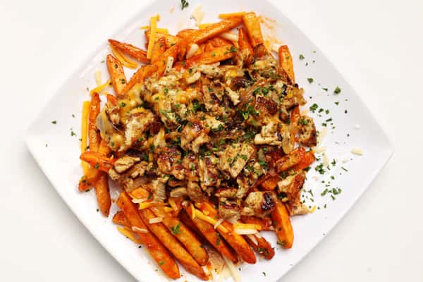 A plate of Nashville hot chicken and sweet potato fries is shown. The fries are topped with cheese and chopped chicken and garnished with parsley.