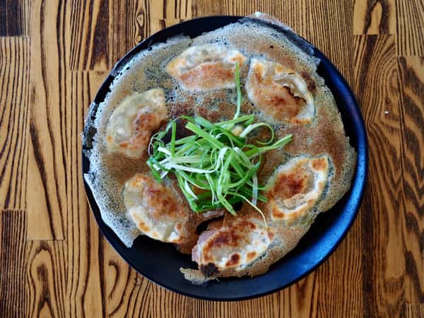 Pan-fried dumplings arranged in a circular pattern topped with sliced scallions