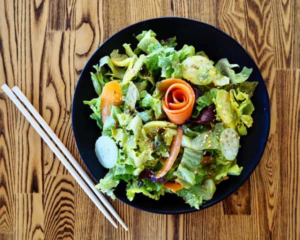 Fresh green salad with lettuce, cucumber, and a carrot rose on a black plate with chopsticks