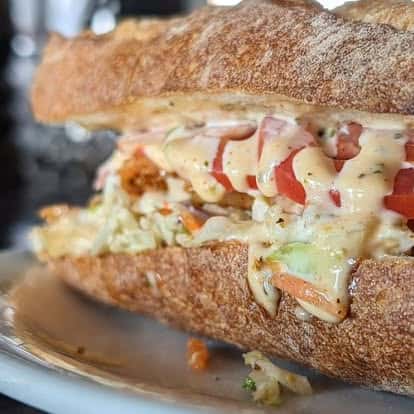 Toasted sandwich stuffed with fresh tomatoes, shredded vegetables, and drizzled with creamy sauce on a white plate.