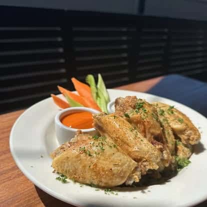 Plate of seasoned chicken wings with carrot and celery sticks, served with a side of buffalo dipping sauce.