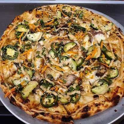 Thin-crust pizza topped with zucchini, jalapeños, onions, carrots, herbs, and melted cheese on a silver serving tray.