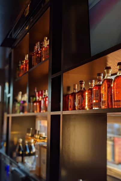 A warmly lit bar shelf stocked with various bottles of liquor, including whiskey, champagne, and spirits, arranged neatly for display.