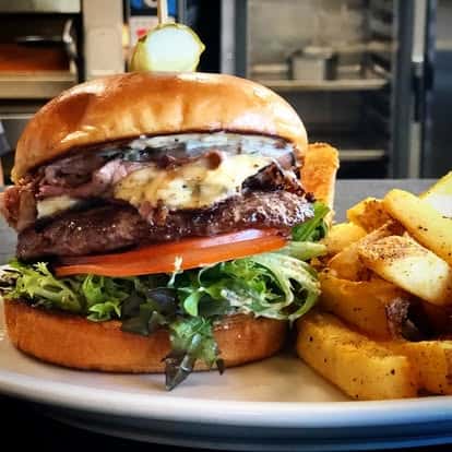 Gourmet burger with lettuce, tomato, melted cheese, and grilled meat, served with seasoned fries on a white plate.