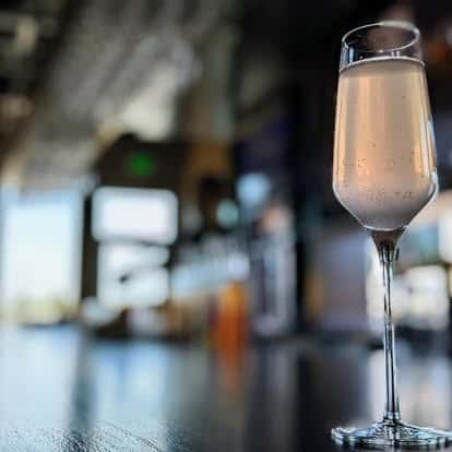 Champagne flute filled with sparkling wine on a reflective bar counter in a softly lit modern bar setting.