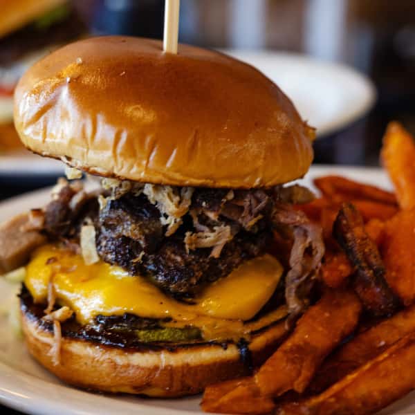 Juicy cheeseburger with shredded meat, cheddar cheese, pickles, and a glossy bun, served with crispy sweet potato fries.