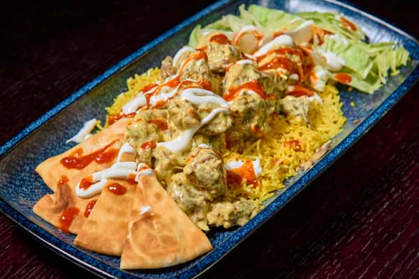 Chicken tikka platter over basmati rice with naan, salad, and creamy sauces