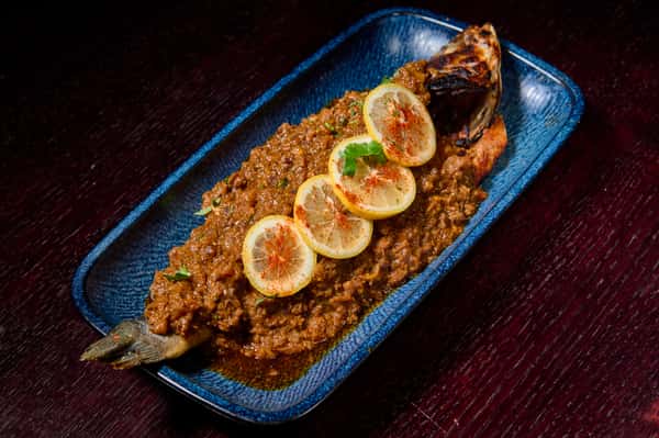 Whole fish in rich spiced masala gravy garnished with lemon slices and herbs