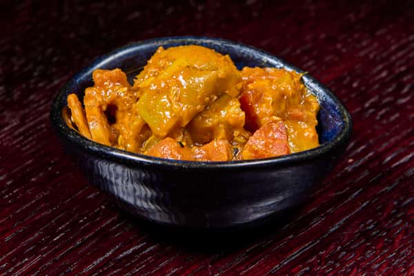 creamy vegetable curry with potatoes and carrots in a rich orange sauce served in a small black bowl