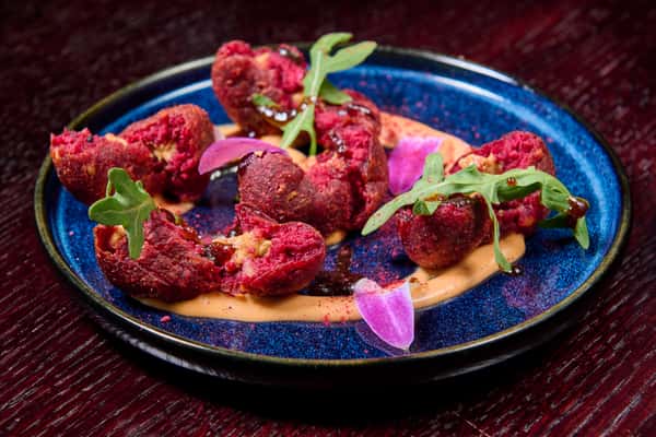Crispy beetroot fritters plated with creamy sauce and fresh greens