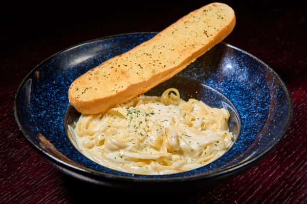 Creamy fettuccine Alfredo pasta topped with herbs and served with garlic bread
