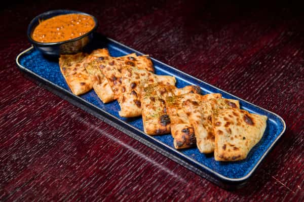 Grilled naan bread slices served with a side of spiced dipping sauce