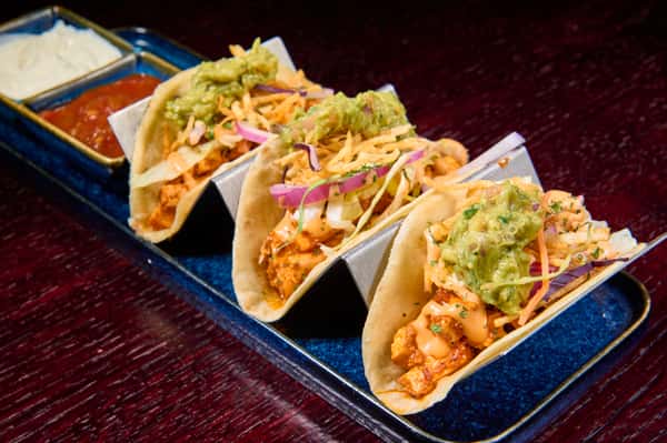 Three chicken tacos topped with slaw and creamy sauce served with dips