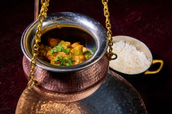 Indian chicken curry served in a hanging copper pot with basmati rice on the side
