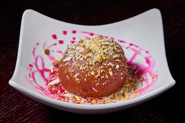 Gulab jamun dessert topped with crushed nuts and rose syrup