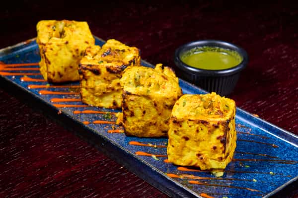 Grilled paneer tikka cubes on a platter with chutney dipping sauce