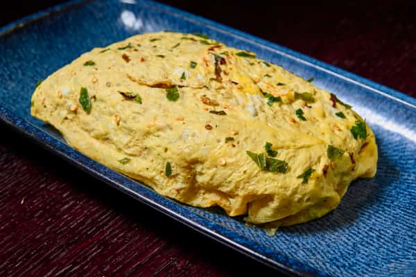 fluffy masala omelette garnished with herbs served on a rectangular plate