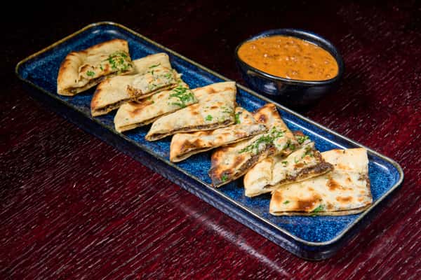 keema naan stuffed flatbread cut into slices served with creamy curry dipping sauce on a blue platter