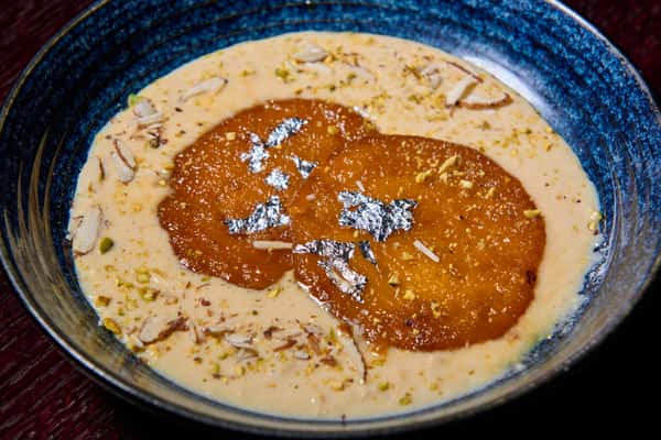 Malpua pancakes soaked in rabri milk and garnished with silver leaf and nuts