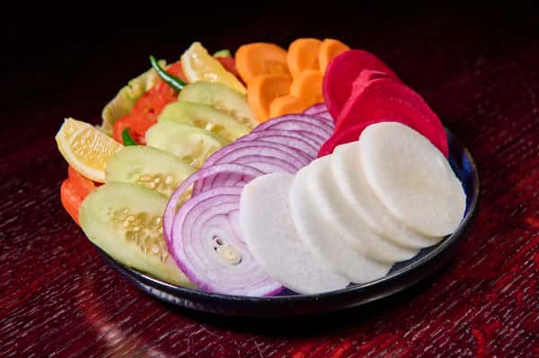 Fresh sliced salad with cucumber, onion, radish, carrot, and lemon wedges
