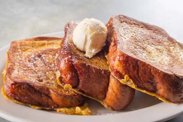 Thick slices of golden French toast topped with a scoop of butter and dusted with powdered sugar.