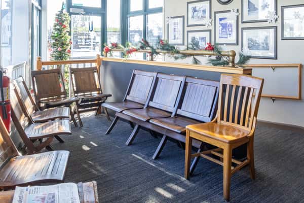 Restaurant waiting area with wooden chairs, framed black-and-white photos, holiday garland, and a decorated Christmas tree.