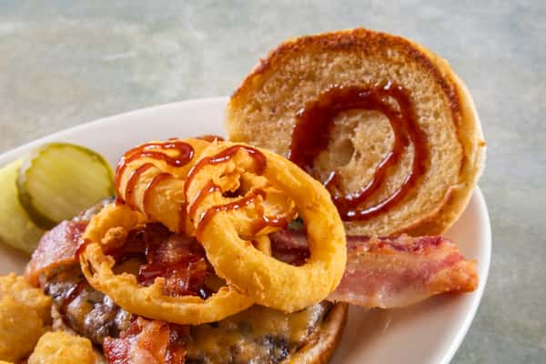 Cheeseburger topped with crispy bacon, onion rings, and barbecue sauce, served with pickle slices and tater tots.