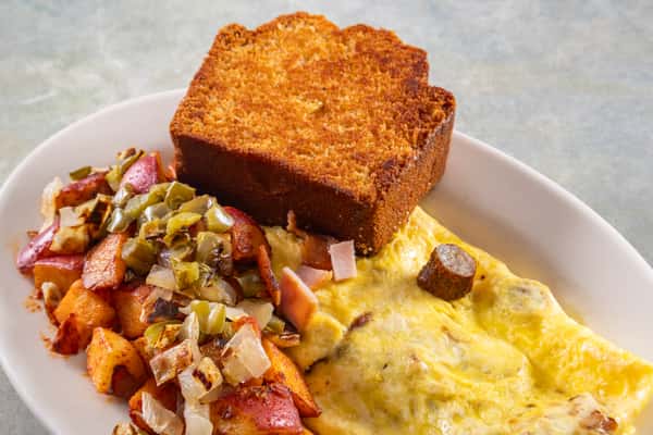 Cheesy sausage omelet served with grilled potatoes topped with onions and peppers, and a thick slice of toasted cornbread.