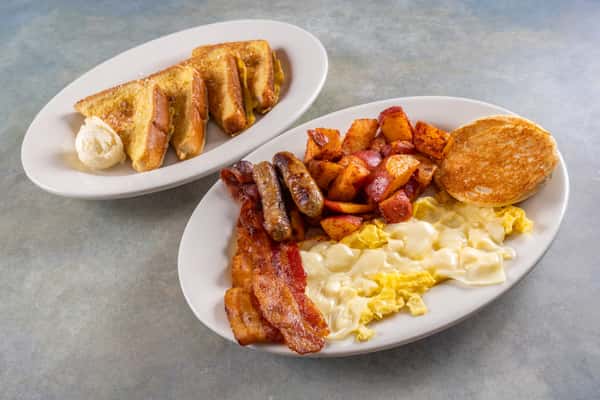 Classic breakfast plate with scrambled eggs and melted cheese, breakfast potatoes, sausage, bacon, and toast, served with French toast.