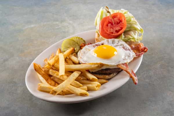 This dish features a hearty breakfast-style burger topped with a sunny-side-up egg, crispy bacon, lettuce, tomato, and pickles, served with a generous portion of golden French fries.
