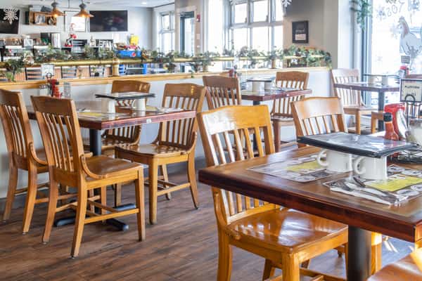 Bright and cozy diner interior with wooden chairs, set tables, festive holiday garlands, and large windows letting in natural light.