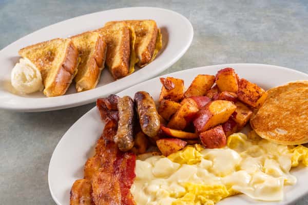 Classic breakfast plate with scrambled eggs and melted cheese, breakfast potatoes, sausage, bacon, and toast, served with French toast.