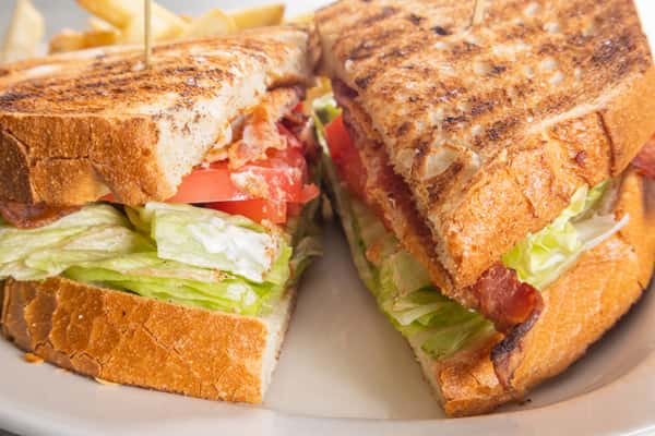 Close-up of a toasted BLT sandwich with crispy bacon, fresh lettuce, and tomato slices, served with a side of French fries.