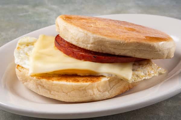 Toasted English muffin breakfast sandwich with egg, melted cheese, and a thick slice of grilled meat.