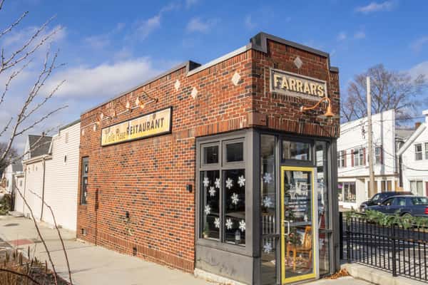 Brick building exterior of Nellie Rose Restaurant with a vintage Farrar's sign, large windows, and festive snowflake decals.