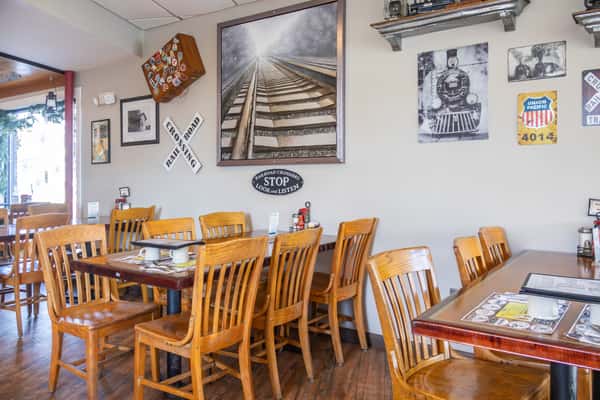 This diner features a charming railroad theme, with train memorabilia and vintage signage adorning the walls, along with cozy wooden seating and tables set for breakfast.
