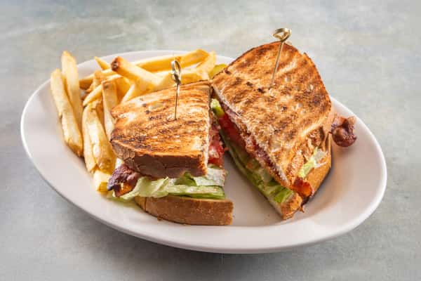 This image shows a toasted BLT sandwich (bacon, lettuce, and tomato) served with a side of golden French fries. The sandwich is secured with skewers and looks freshly grilled.