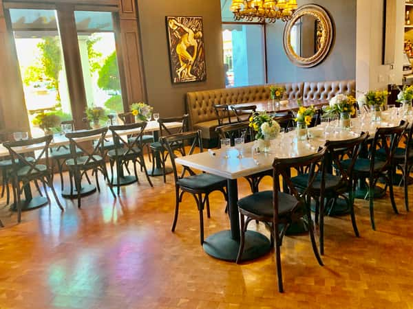 Elegant restaurant dining room with set tables, floral centerpieces, chandelier, and tufted booth seating by large windows