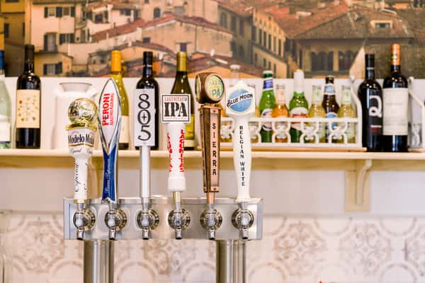 Row of beer taps including Modelo, Peroni, Lagunitas IPA, Sierra Nevada Hazy IPA, and Blue Moon at bar counter with wine bottles behind
