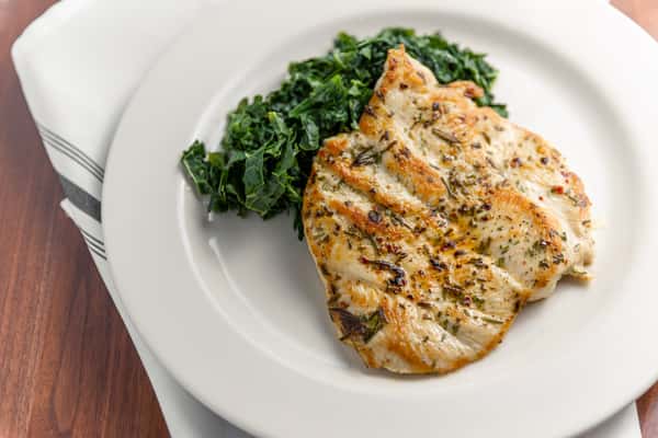 Grilled herb-seasoned chicken breast served with sautéed greens on a white plate.